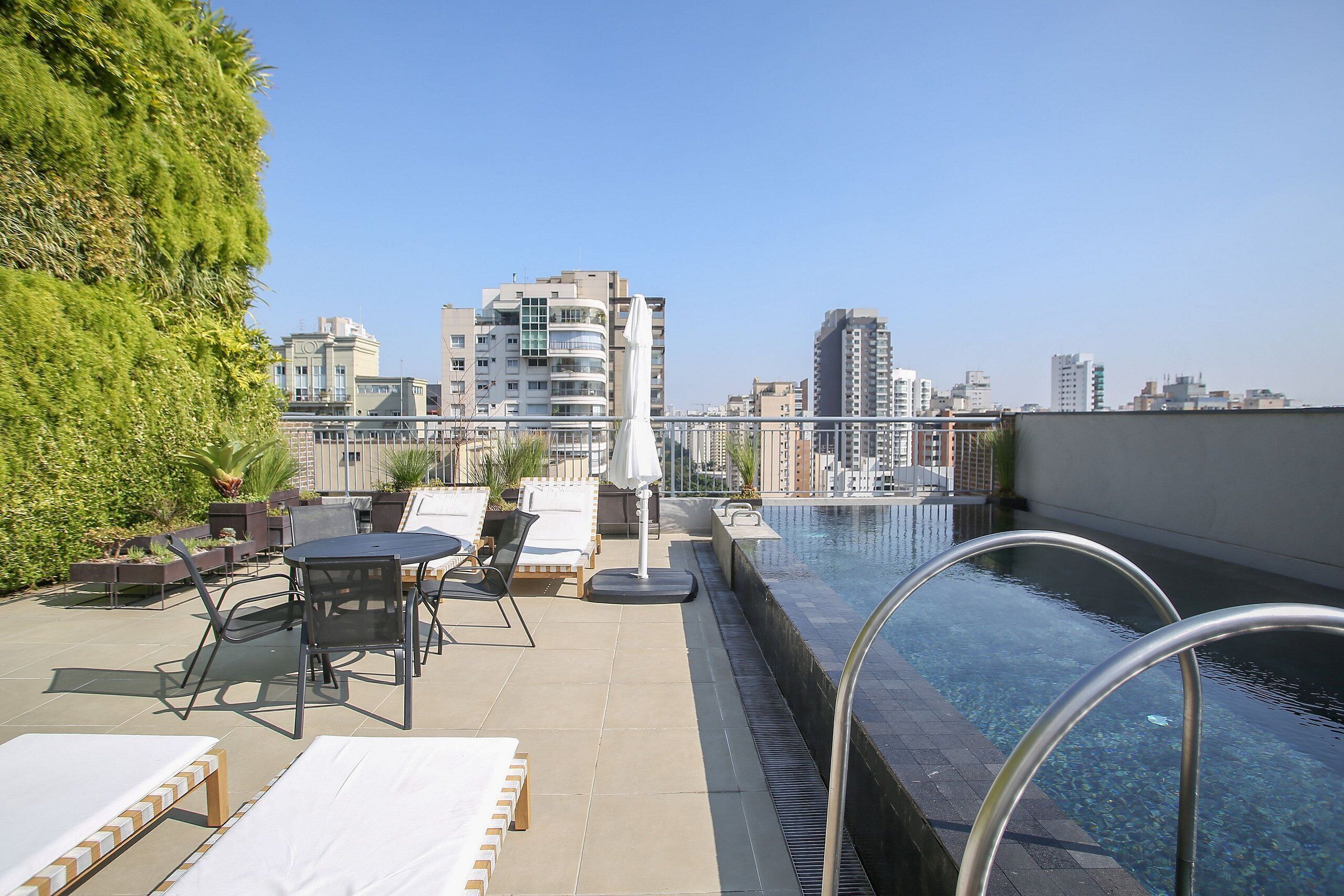 Un área de piscina en la azotea con sillones, una mesa y vistas de la ciudad.