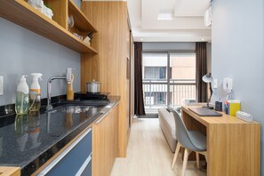 Une cuisine moderne avec un plan de travail noir, des armoires en bois et une fenêtre donnant sur des immeubles.