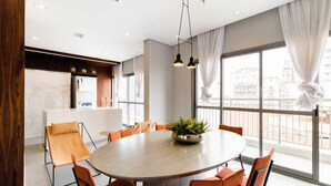 Une salle de conférence moderne, dotée d’une table ronde, de chaises orange, d’une plante en pot et de grandes fenêtres avec des rideaux.