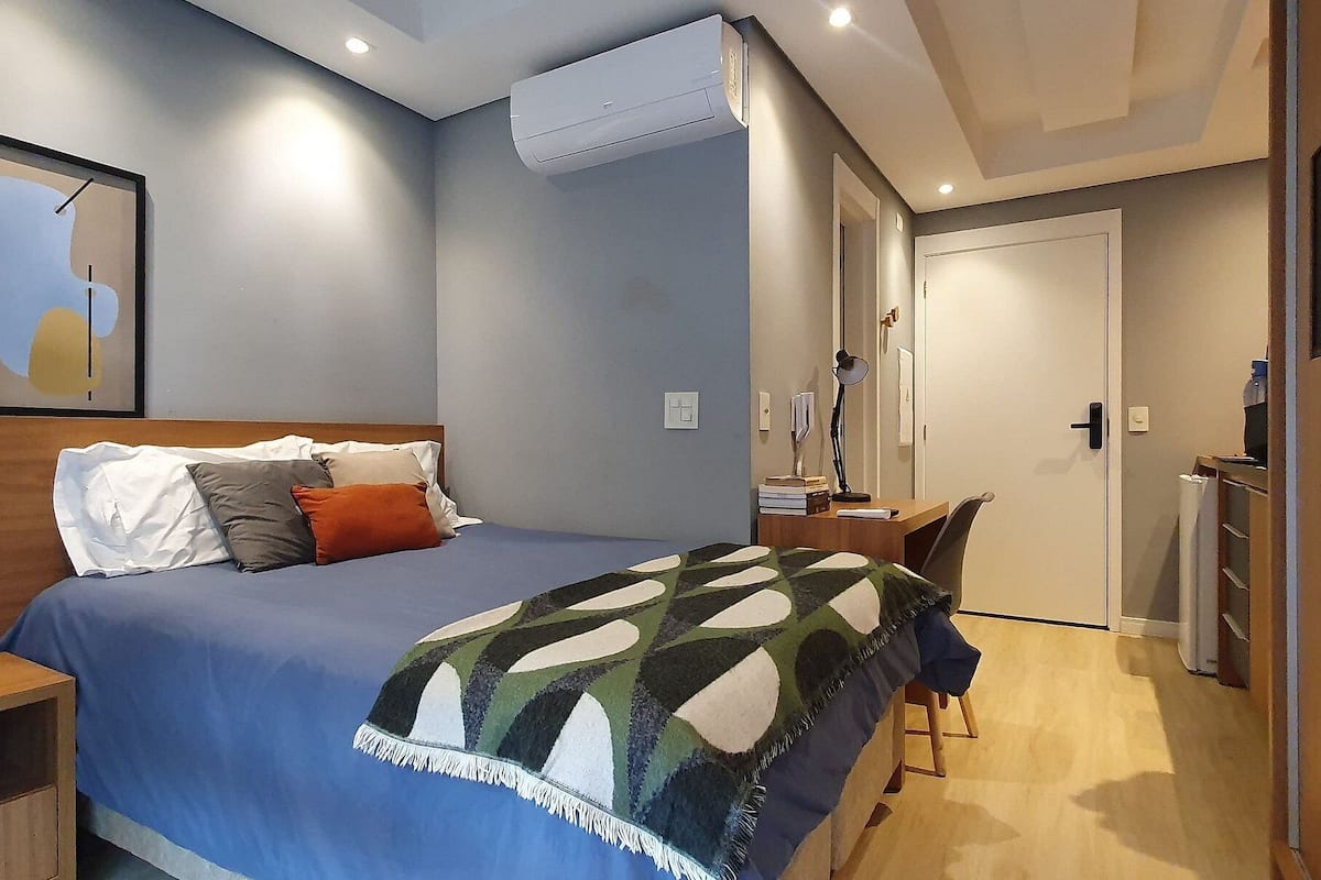 Ein Schlafzimmer mit Bett, Nachttisch, Schreibtisch, Stuhl und Klimaanlage.