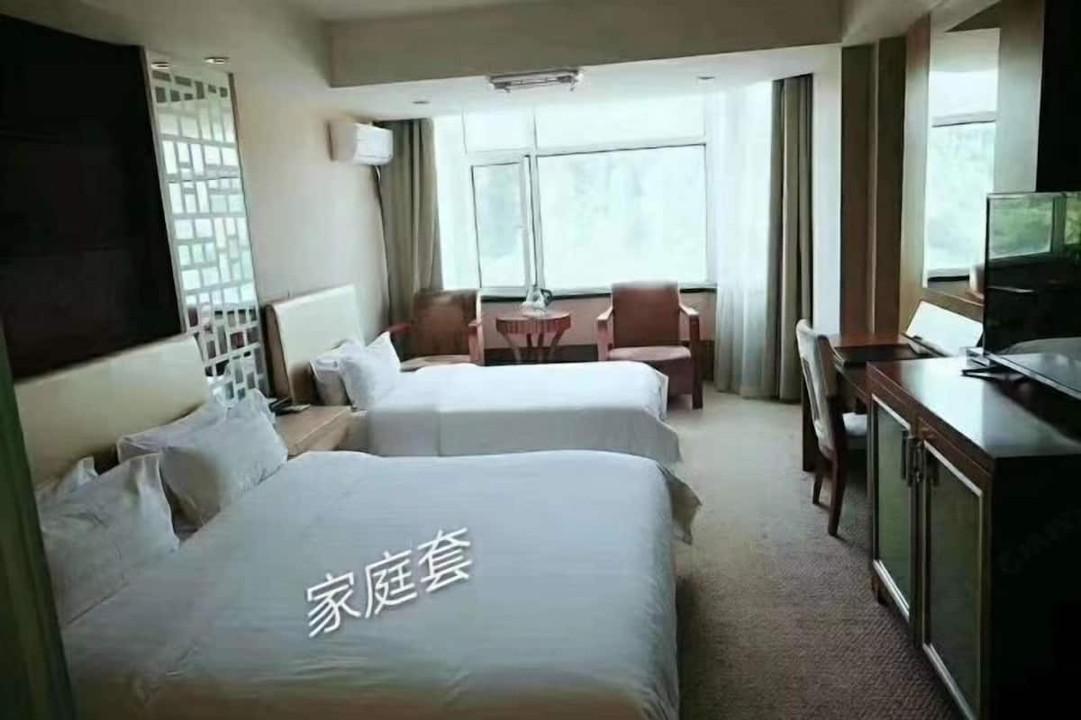 Een hotelkamer met twee bedden, een bureau, een stoel, een televisie en een raam met gordijnen.