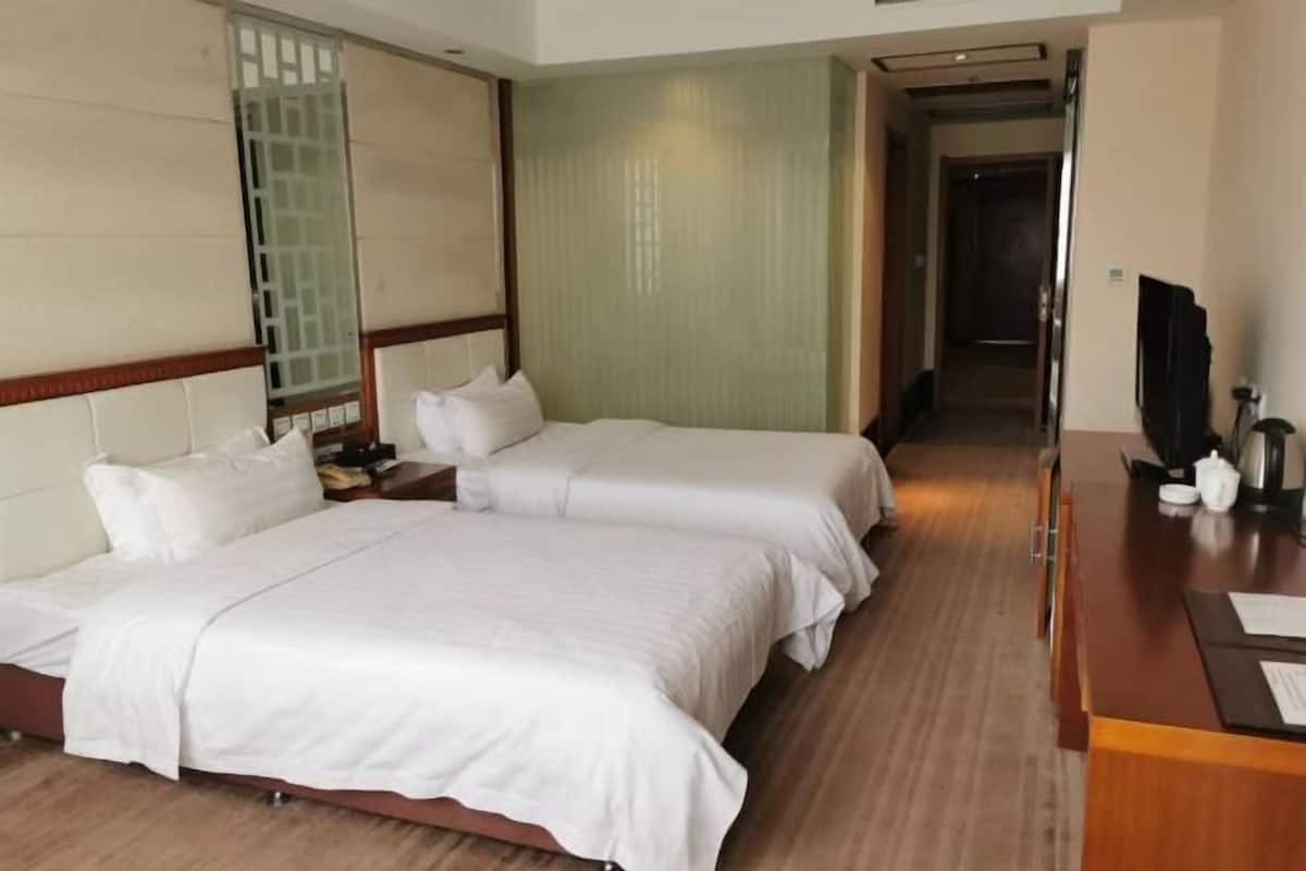 Een hotelkamer met twee bedden, een houten vloer, een bureau met een televisie en een schuifdeur.