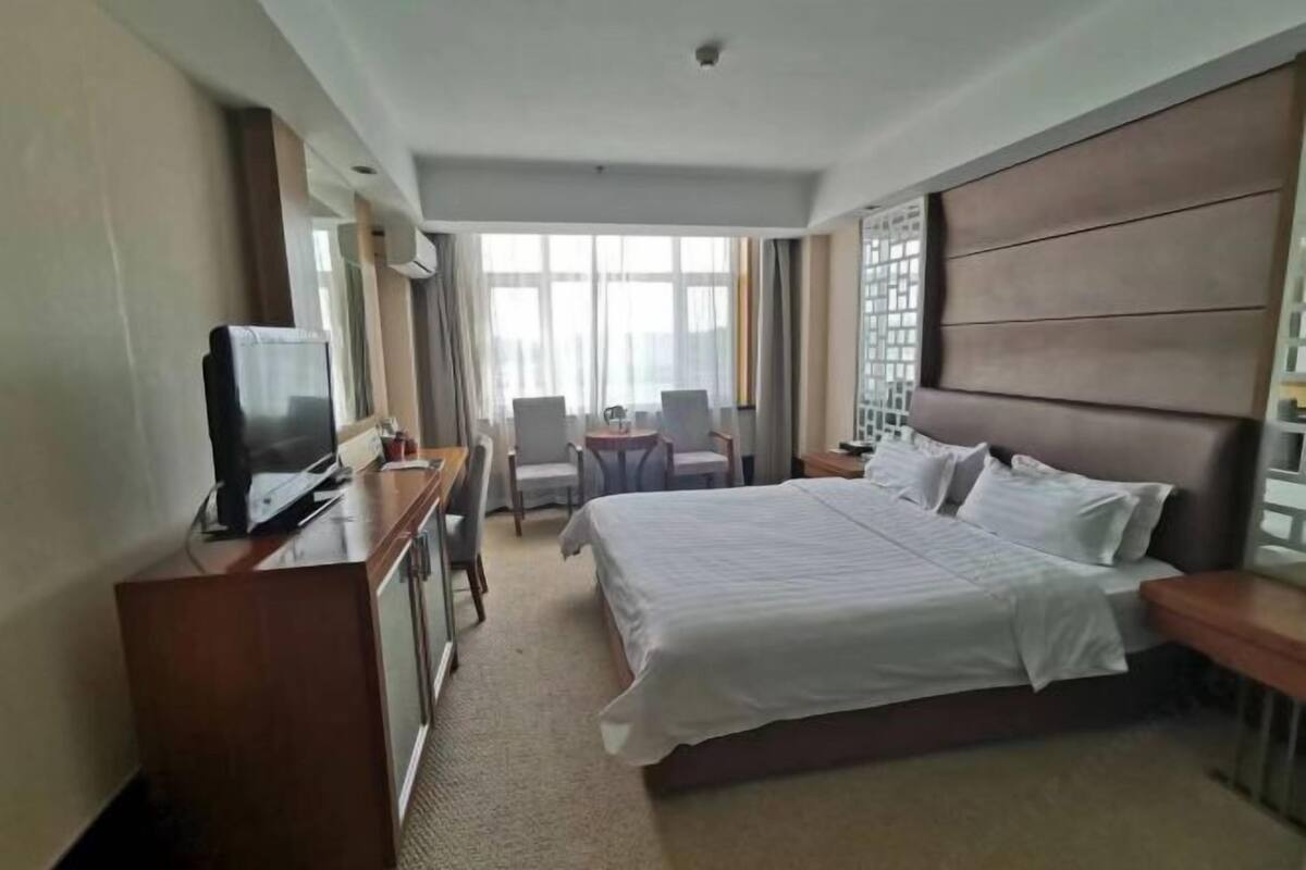 Hotelkamer met een groot bed, een bureau met een televisie en een zithoek met stoelen en een kleine tafel.