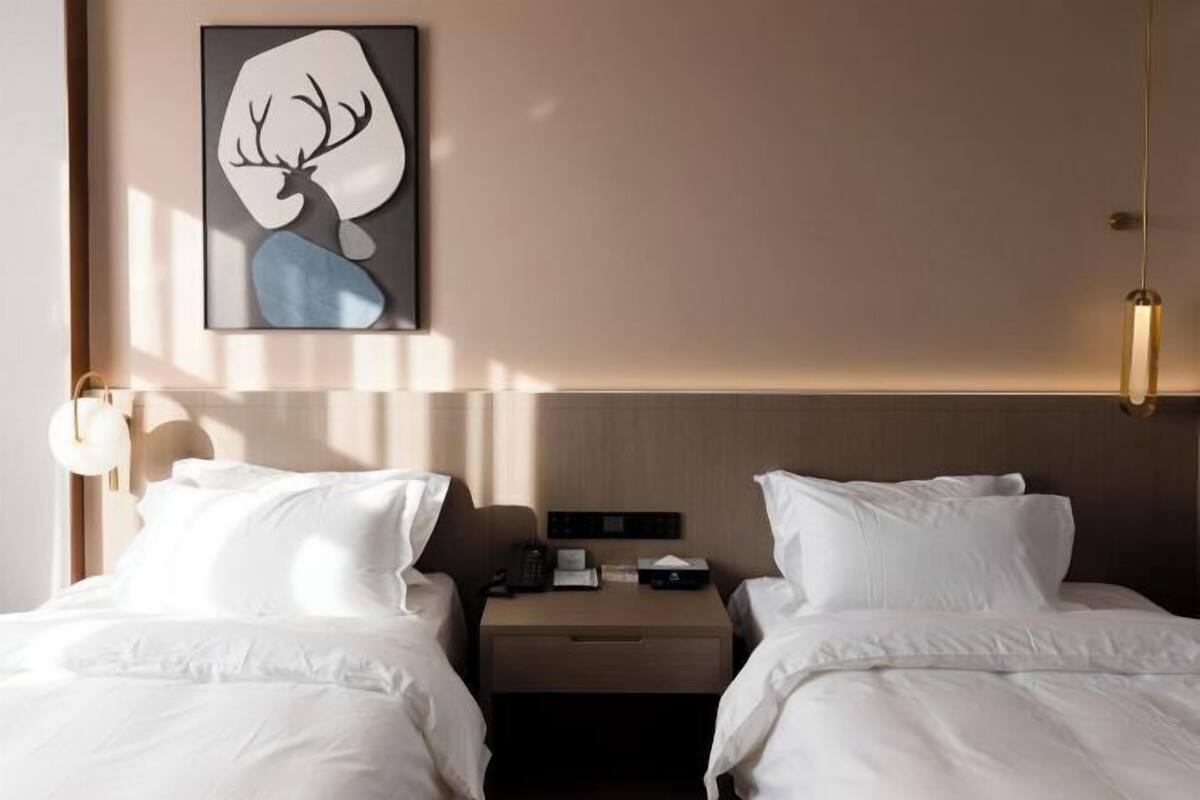 Een hotelkamer met twee bedden, een nachtkastje, een aan de muur hangend kunstwerk en een lamp.