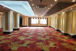 Un salón amplio y vacío con alfombra estampada, columnas y una pared larga con ventanas.