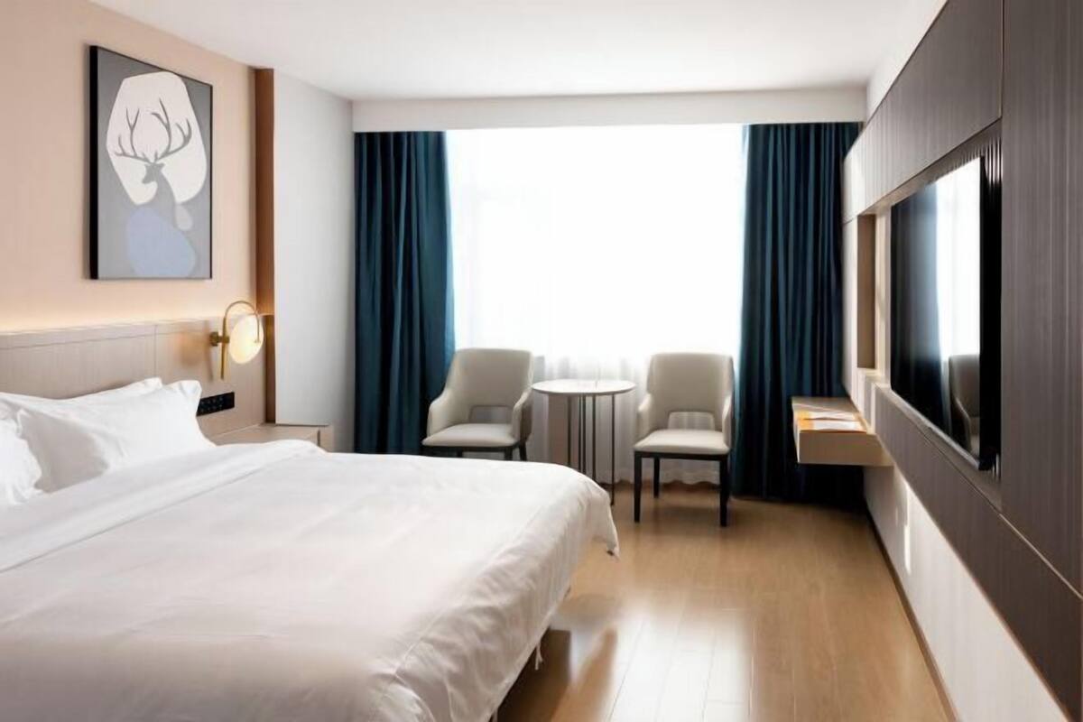 Een hotelkamer met een groot bed, twee fauteuils, een tafeltje, een televisie en een schilderij aan de muur.