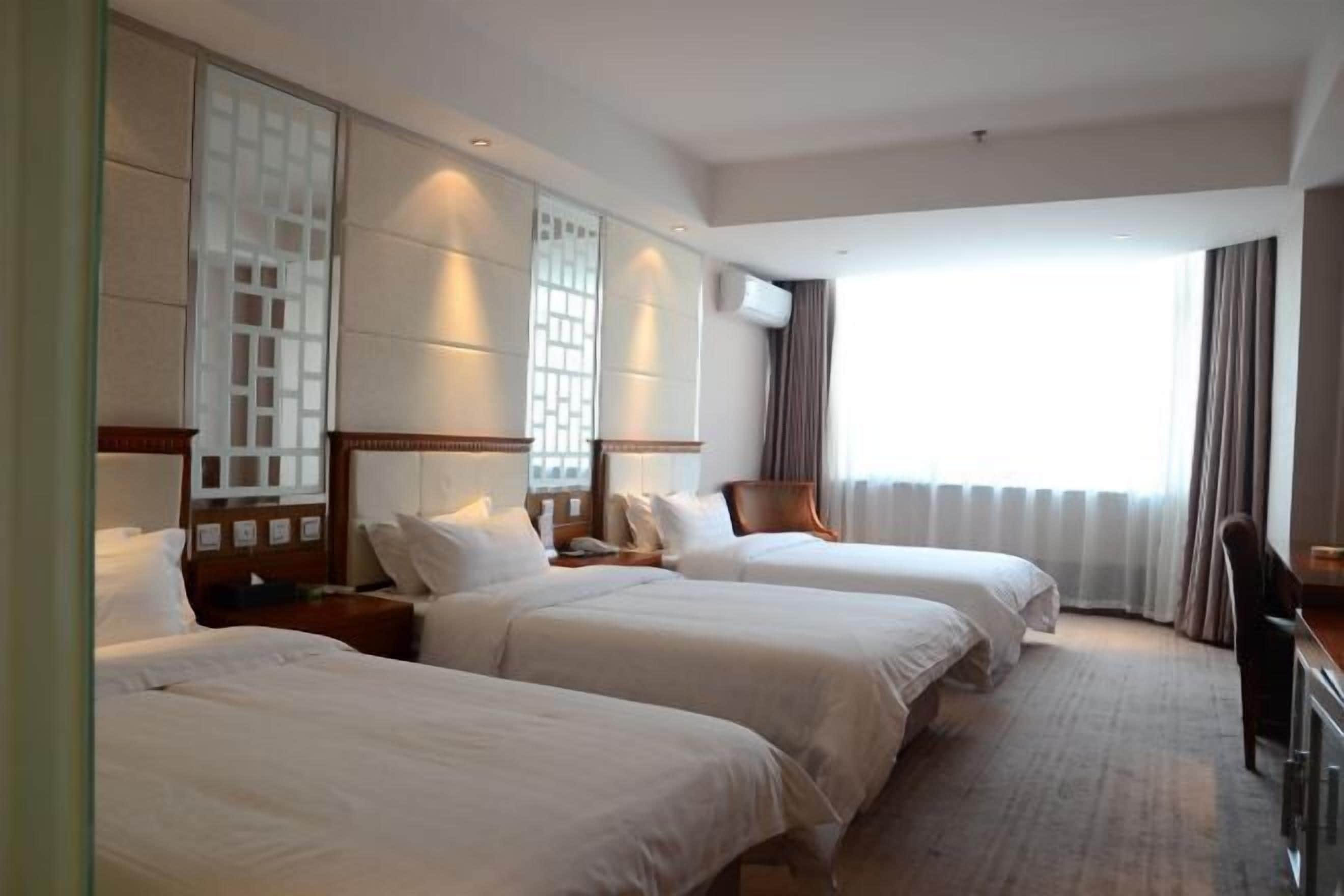 A hotel room with two beds, a desk, and a large window with curtains.