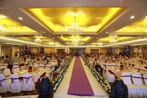 Une salle de banquet avec des rangées de tables, une allée centrale et des lustres.