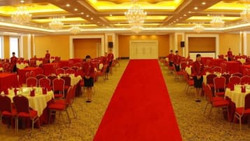 A banquet hall with round tables, a red carpet, and chandeliers.