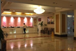 A hotel lobby with a reception desk, seating area, and a large chandelier.