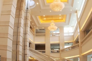 Un interior de varios niveles con una imponente escalera, candelabros y un techo alto.