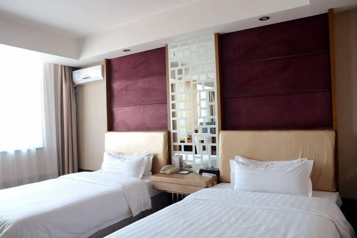 Een hotelkamer met twee bedden, een houten nachtkastje, een telefoon en een decoratieve scheidingswand.