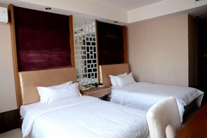 Habitación de hotel con dos camas individuales, cabecero de madera, una mesita de noche pequeña y un separador decorativo blanco.