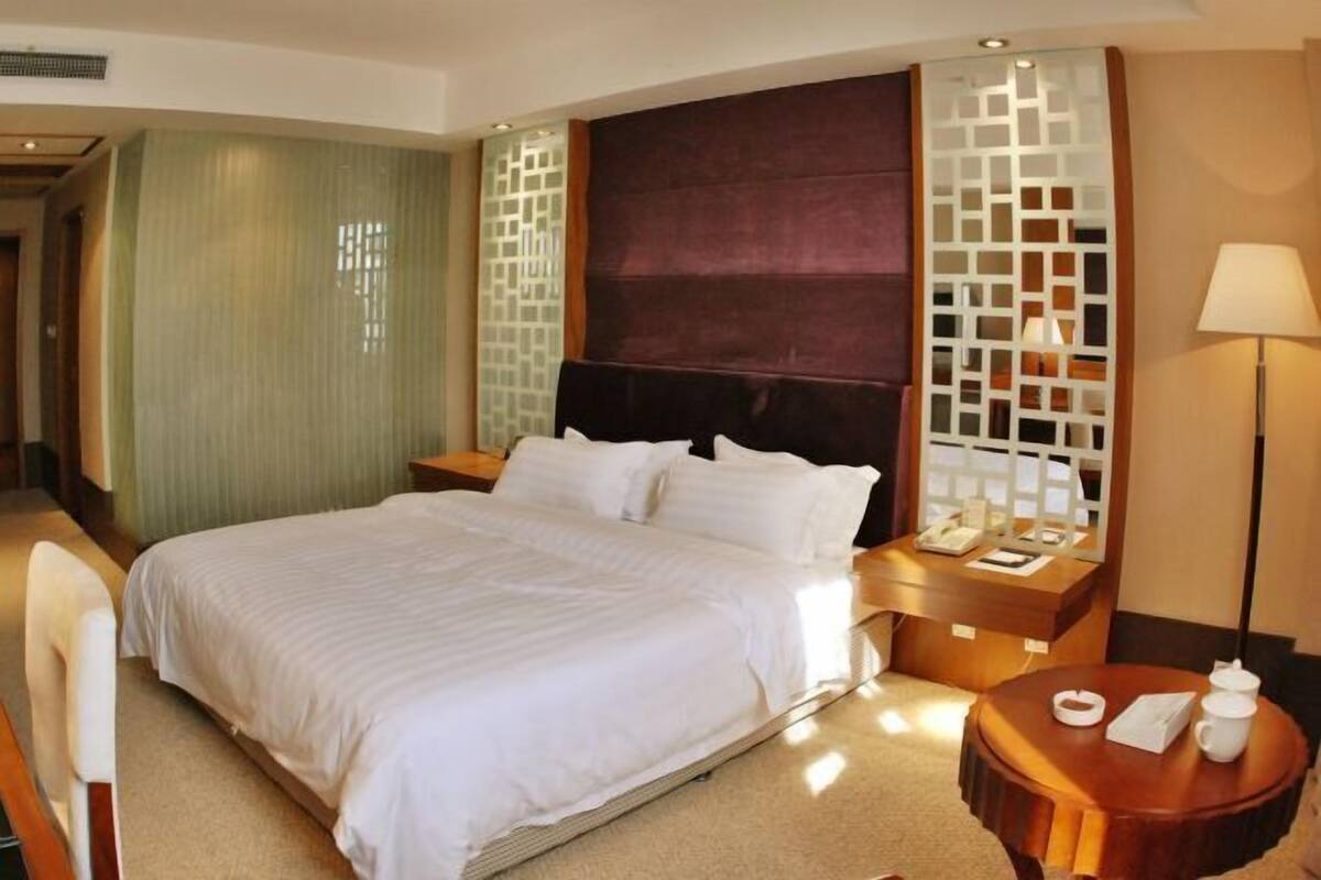Een hotelkamer met een groot bed, een houten nachtkastje, een bureau met een lamp en een stoel.
