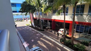 A street view with a building featuring a red and white facade, palm trees, and a parked car.