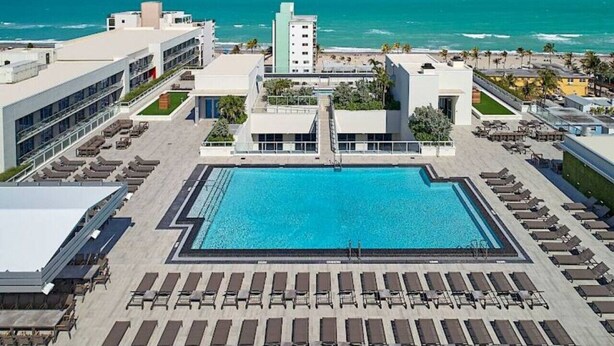 A rooftop pool area with a large pool, sun loungers, and a view of the ocean.