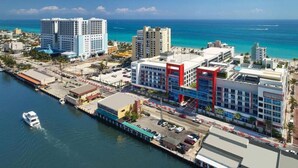 An aerial view of a coastal city with a marina, high-rise buildings, and a prominent red and blue building with a modern design.