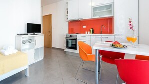 A modern kitchen with white cabinets, a red backsplash, and a dining area with orange chairs. - Apartments Gulin - One Bedroom Apartment with Terrace and Sea View (Šibenik)