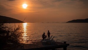 Ein Sonnenuntergang über ruhigem Wasser, mit einem Steg und Stühlen.