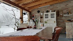 Un coin repas rustique, avec une table en bois, un mur en briques, un buffet blanc aux portes vitr ées et une vue sur un paysage enneigé.