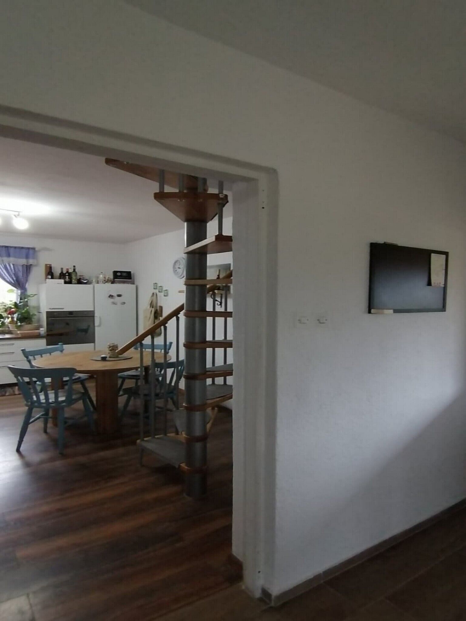 A kitchen with a dining area, wooden staircase, and a TV mounted on the wall.