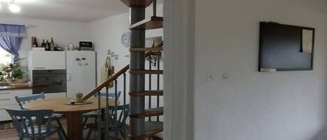 A kitchen with a dining area, wooden staircase, and a TV mounted on the wall.
