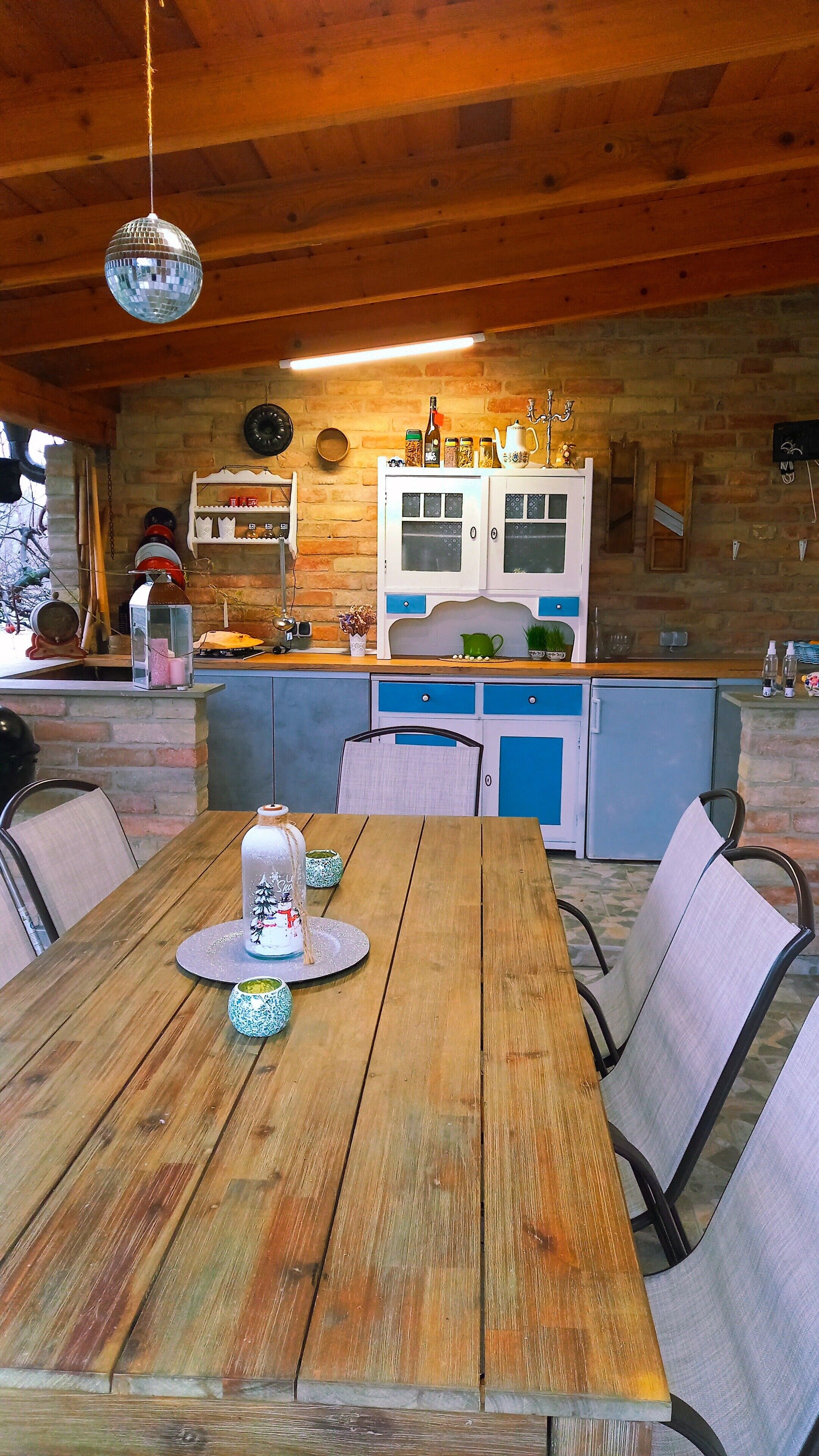 Une table à manger en bois avec des chaises, un coin cuisine avec des meubles bleus et une boule à facettes suspendue au plafond.