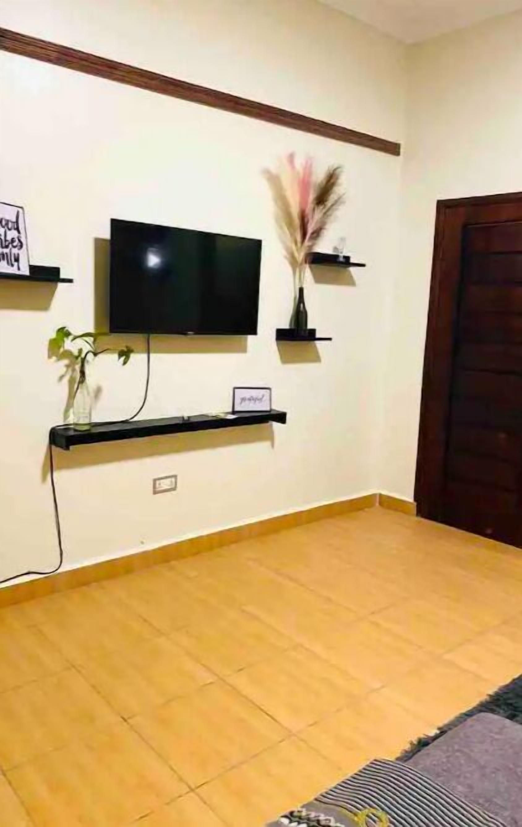 Een woonkamer met een flatscreen televisie aan de muur, een houten deur en een betegelde vloer.
