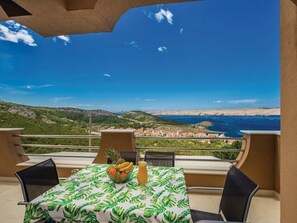 A table with a tropical leaf tablecloth, two chairs, a fruit bowl with bananas and oranges, and a glass of orange juice.