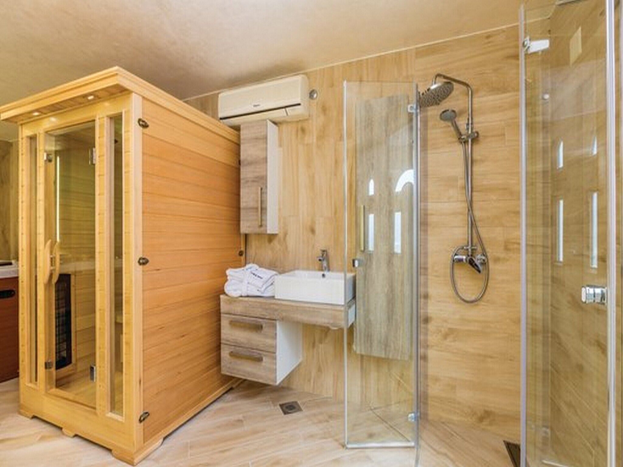 Een moderne badkamer met een houten kast, een douchecabine met glazen wanden en een wastafel met handdoeken.