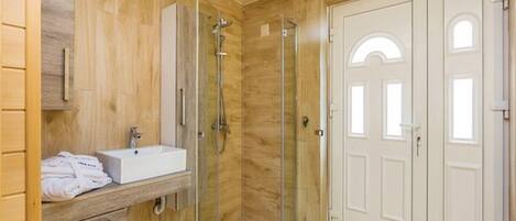 A modern bathroom with a wooden vanity, a glass shower enclosure, and a white door.