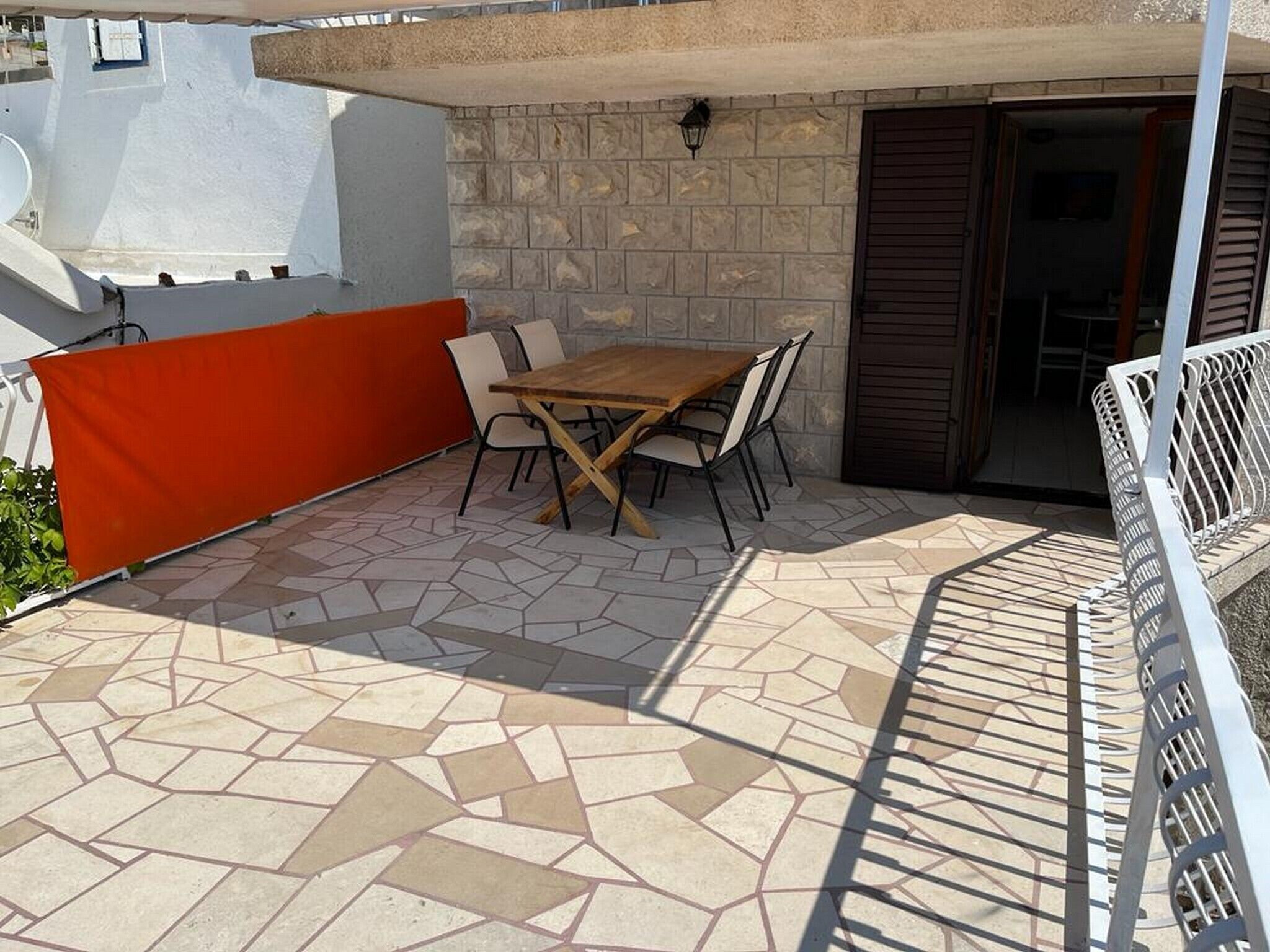 Une terrasse avec un sol carrelé en pierre, une table en bois et des chaises.