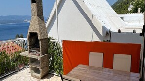 An outdoor patio with a stone-built grill, a table with chairs, and a view of the sea. - Apartments Leut - One-Bedroom Apartment with Terrace and Sea View (Pisak)