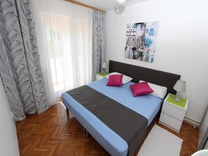 A bedroom with a bed, a nightstand, a wall art piece, and a window with curtains.
