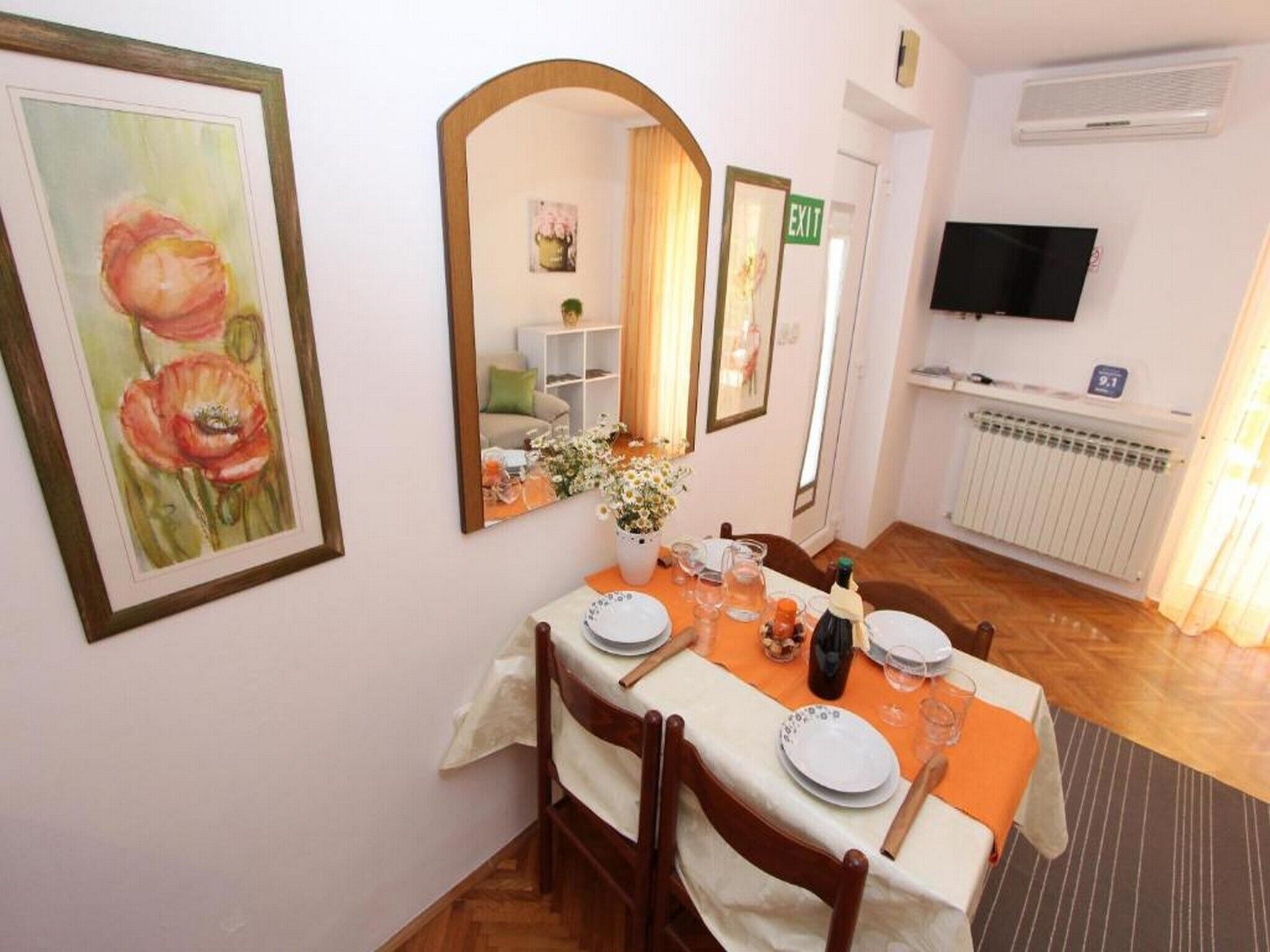 A dining area with a table set for four, a mirror, a television, and an exit sign.