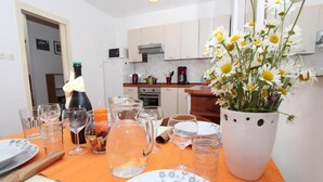 Eine Küche mit weißen Schränken, einer Mikrowelle und einer Kaffeemaschine. Ein Tisch mit Blumen in einer Vase, Gläsern und Tellern.