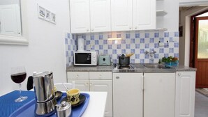 A compact kitchen with white cabinets, a microwave, a kettle, and a toaster. There is a window with a view of greenery outside. - Apartments Frane - One Bedroom Apartment with Terrace (Rovinj)