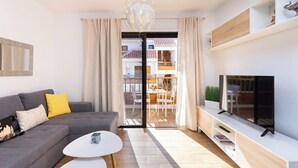 A modern living room with a grey sofa, white coffee table, and a flat-screen TV on a white TV stand.
