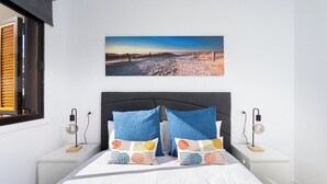 A bedroom with a bed, two nightstands, a wall-mounted picture, and a window with blinds.