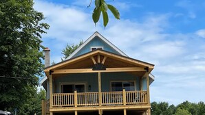 A large, single-story house with a wooden porch and a covered front porch area. - Equestrian Charm near Torch Lake: Two homes in one! (Rapid City)