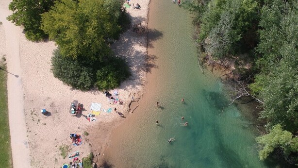 An aerial view of a beach with people swimming and sunbathing, surrounded by greenery. - Equestrian Charm near Torch Lake: Two homes in one! (Rapid City)