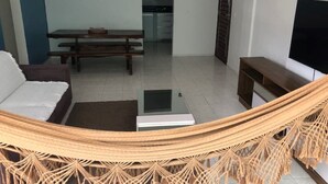 Un salon avec un hamac, un canapé, une télévision et, au fond, un coin repas.