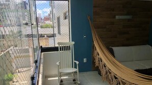 Une pièce avec un hamac, une chaise blanche et une vue sur l’extérieur, visible à travers une porte vitrée.