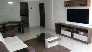 Un salon moderne avec un téléviseur à écran plat fixé au mur, un meuble de rangement en bois, une table basse en verre et un canapé agrémenté d’un tapis décoratif.
