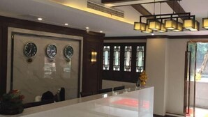 Un hall d’hôtel moderne avec un comptoir d’accueil en marbre, des horloges murales et des fenêtres de style traditionnel.