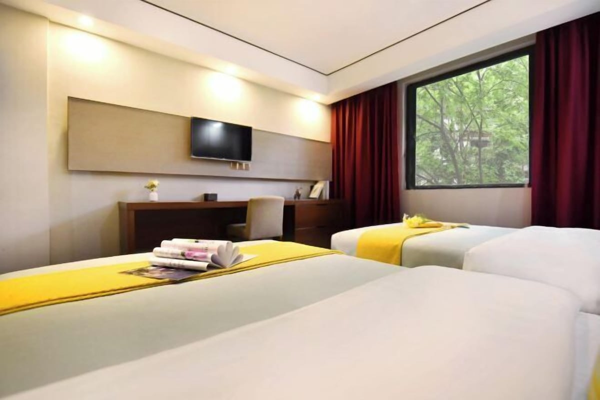 Habitación de hotel con dos camas, un escritorio, un televisor y una ventana con cortinas.