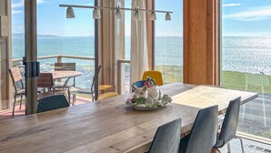 A dining area with a large table and chairs, a decorative ceramic plate, and a view of the ocean through large windows. - Ocean Atrium - Amazing Frontline Views (Bodega Bay)