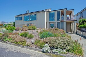 A modern two-story house with large windows, a balcony, and a well-maintained garden with various plants and flowers. - Ocean Atrium - Amazing Frontline Views (Bodega Bay)