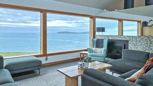 A modern living room with large windows, a fireplace, and a view of the sea. - Ocean Atrium - Amazing Frontline Views (Bodega Bay)