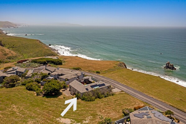 An aerial view of a coastal residential area with houses, a road, and the ocean. - Ocean Atrium - Amazing Frontline Views (Bodega Bay)